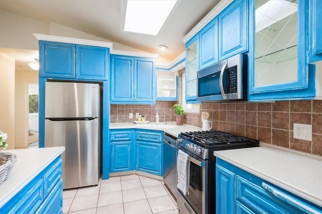 kitchen with decorative backsplash, vaulted ceiling with skylight, stainless steel appliances, blue cabinetry, and light tile patterned flooring