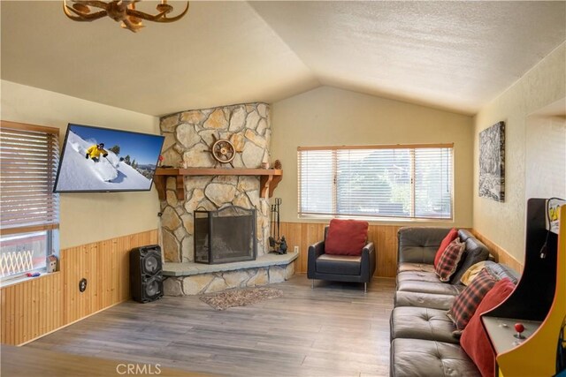 living room with lofted ceiling, a stone fireplace, a textured ceiling, wooden walls, and hardwood / wood-style flooring