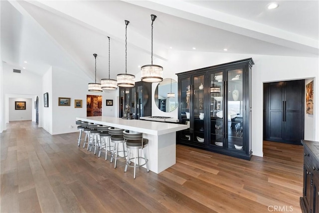 kitchen with a kitchen island with sink, high vaulted ceiling, dark hardwood / wood-style floors, decorative light fixtures, and a kitchen bar