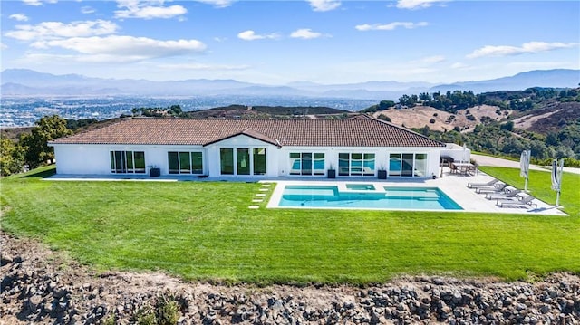 rear view of property with a lawn, a mountain view, and a patio area