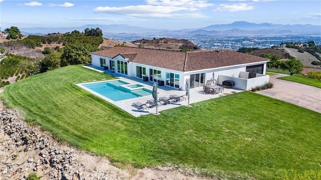 back of property with a mountain view, a patio area, and a lawn