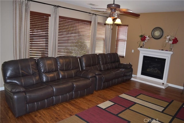 living room featuring a glass covered fireplace, wood finished floors, visible vents, and baseboards