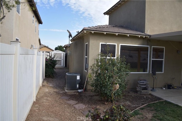 view of property exterior with a tile roof, fence, central AC unit, and stucco siding