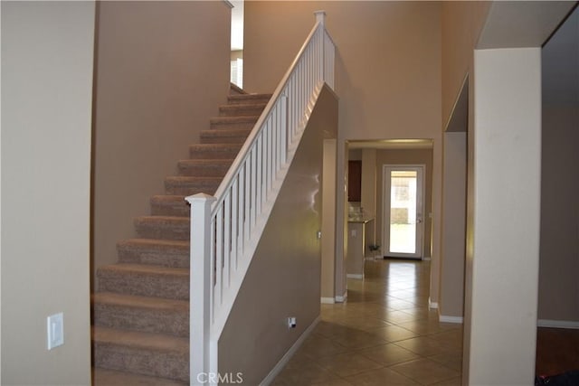 staircase featuring a towering ceiling, tile patterned flooring, and baseboards