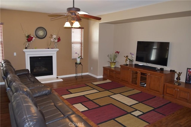 living area with ceiling fan, baseboards, wood finished floors, and a glass covered fireplace