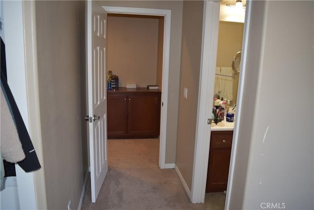 hallway with baseboards and light colored carpet