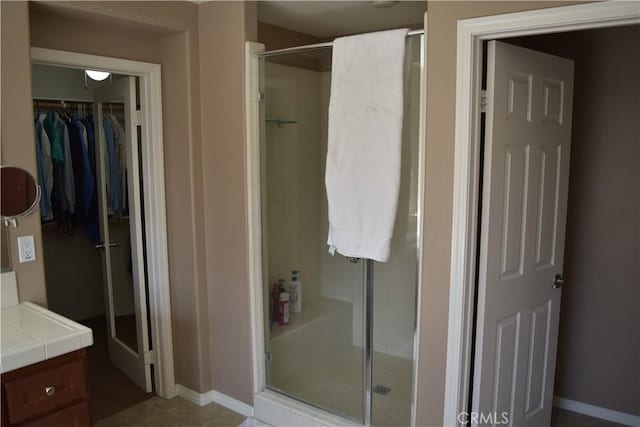 bathroom with a spacious closet, a shower stall, vanity, and baseboards