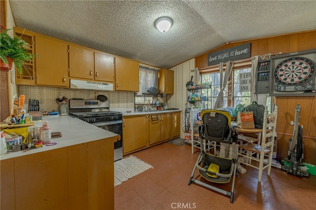 kitchen featuring a textured ceiling, lofted ceiling, wood walls, and stainless steel range oven