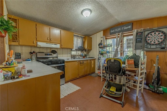 kitchen with under cabinet range hood, stainless steel gas stove, light countertops, lofted ceiling, and light floors