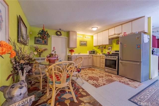 kitchen featuring a textured ceiling, appliances with stainless steel finishes, light countertops, under cabinet range hood, and light floors