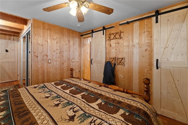 unfurnished bedroom with wood-type flooring, a barn door, ceiling fan, and wood walls