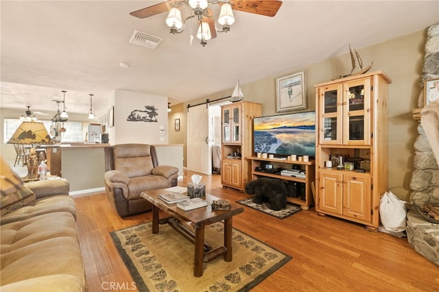 living room with a barn door, ceiling fan, and light hardwood / wood-style floors