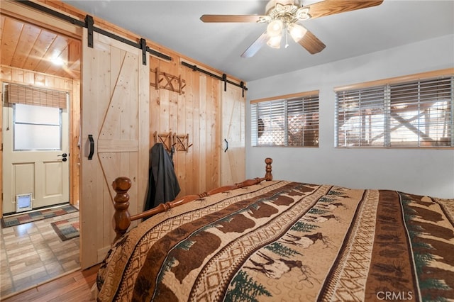 bedroom with wood-type flooring, a barn door, ceiling fan, and wood walls