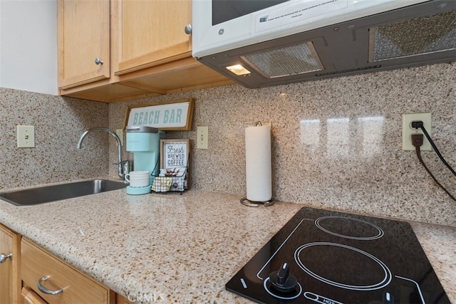 kitchen featuring black electric cooktop, backsplash, light stone countertops, light brown cabinetry, and sink