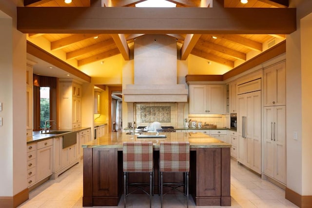 kitchen featuring premium range hood, a kitchen breakfast bar, paneled built in fridge, light stone countertops, and a center island with sink