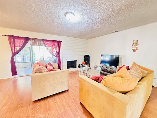 living room featuring a textured ceiling, a large fireplace, and wood-type flooring