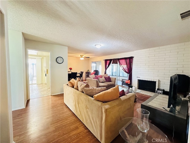 living room featuring a brick fireplace, a textured ceiling, light hardwood / wood-style floors, and ceiling fan