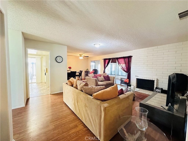 27358 Comwell St, Menifee, CA 92586 - living room with a brick fireplace, a textured ceiling, a ceiling fan, wood finished floors, and visible vents