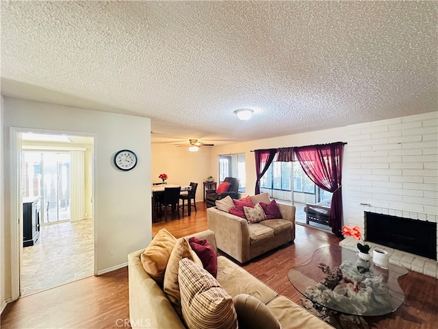 living room featuring ceiling fan, hardwood / wood-style flooring, a textured ceiling, and a fireplace