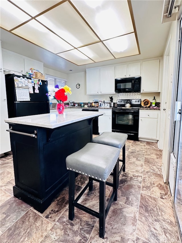 kitchen with a breakfast bar area, black appliances, white cabinets, and a center island