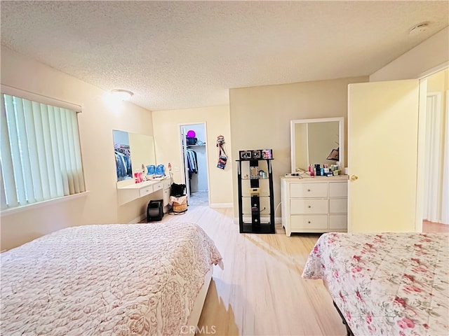 bedroom with a spacious closet, light hardwood / wood-style flooring, a textured ceiling, and a closet