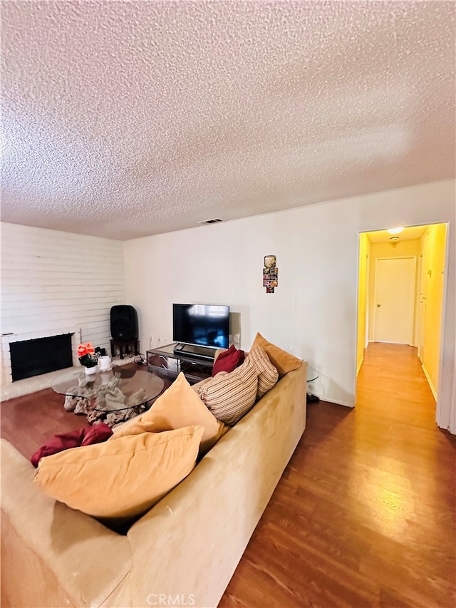 living room featuring a textured ceiling, hardwood / wood-style flooring, and a brick fireplace