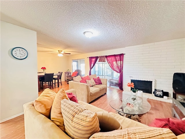 living room with ceiling fan, a textured ceiling, a fireplace, and hardwood / wood-style floors