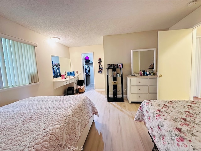 bedroom with a textured ceiling, light hardwood / wood-style floors, a walk in closet, and a closet