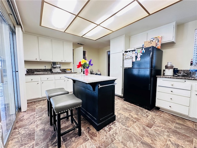 kitchen with white cabinets, a center island, black refrigerator, and a kitchen bar