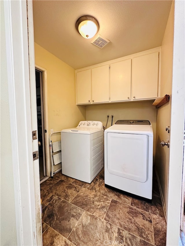 washroom with cabinets, a textured ceiling, and washer and clothes dryer