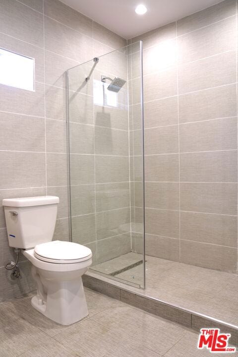 bathroom with a tile shower, tile walls, toilet, and tile patterned floors