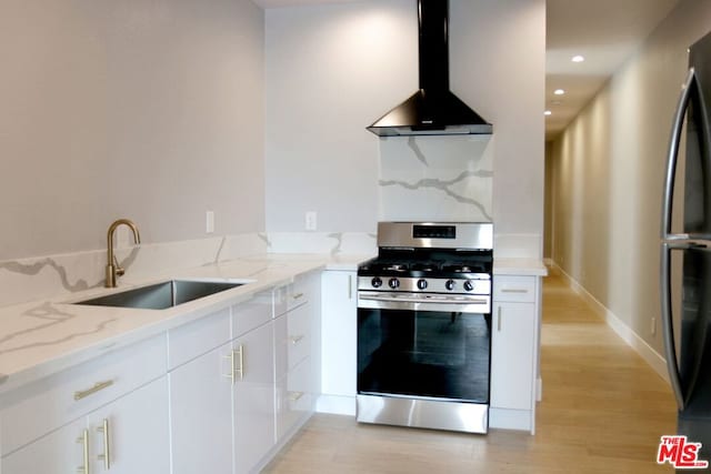 kitchen with appliances with stainless steel finishes, wall chimney range hood, light stone counters, and white cabinets