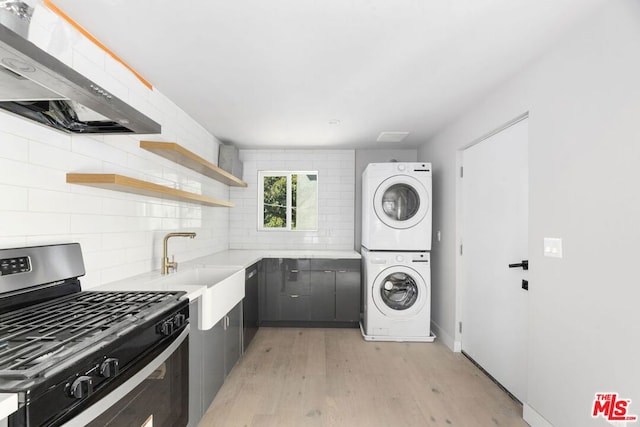 interior space with stacked washer / dryer, stainless steel gas range, exhaust hood, and light hardwood / wood-style flooring