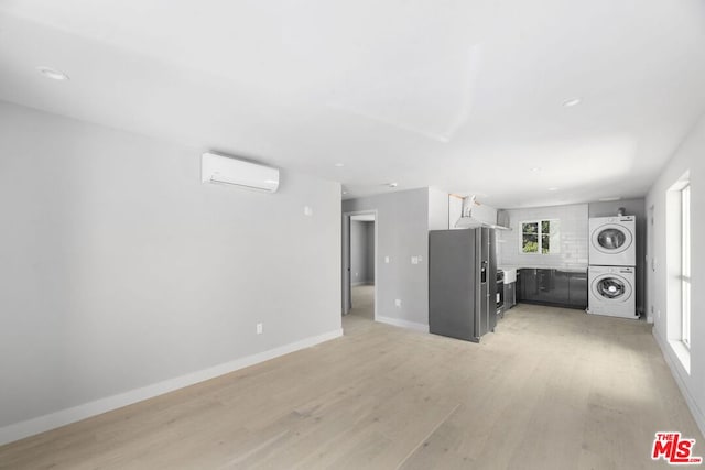 unfurnished living room featuring light wood-type flooring, stacked washing maching and dryer, and a wall mounted AC