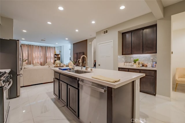 kitchen with backsplash, appliances with stainless steel finishes, a kitchen island with sink, dark brown cabinetry, and sink