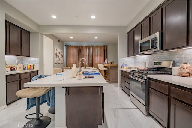 kitchen featuring sink, an island with sink, backsplash, a kitchen breakfast bar, and stainless steel appliances