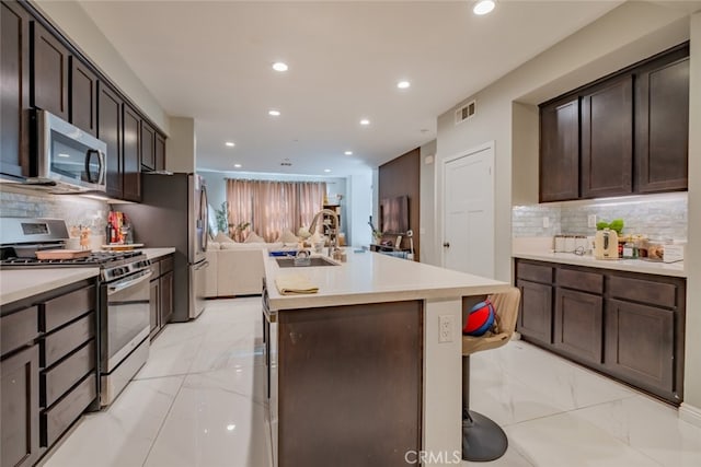 kitchen with sink, appliances with stainless steel finishes, dark brown cabinetry, and backsplash