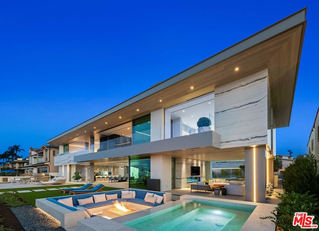 back house at night featuring a balcony, an outdoor living space with a fire pit, and a patio area