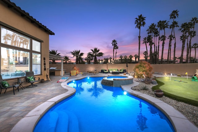 pool at dusk with an in ground hot tub and a patio area