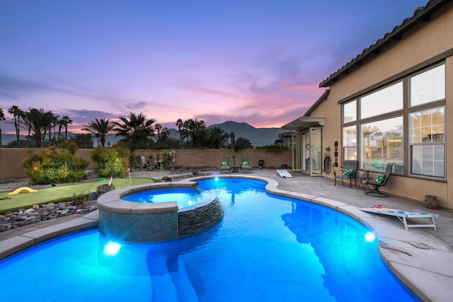 pool at dusk featuring a patio and an in ground hot tub