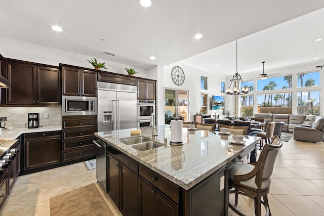 kitchen featuring a breakfast bar, a kitchen island with sink, built in appliances, sink, and decorative backsplash