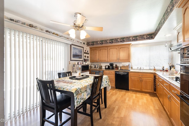 kitchen with a tray ceiling, light stone counters, light hardwood / wood-style floors, black appliances, and ceiling fan