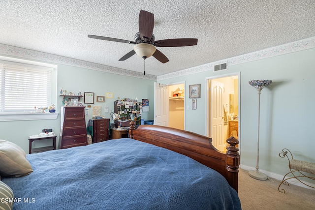 bedroom featuring ceiling fan, a textured ceiling, a walk in closet, carpet floors, and ensuite bathroom