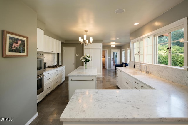 kitchen with light stone counters, hanging light fixtures, white cabinetry, and a kitchen island