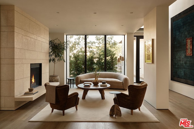 interior space with floor to ceiling windows, a tiled fireplace, and light hardwood / wood-style floors