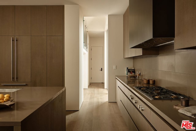 kitchen featuring wall chimney exhaust hood, light hardwood / wood-style floors, tasteful backsplash, and stainless steel gas cooktop