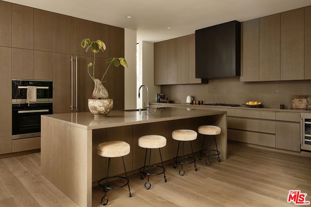 kitchen featuring a kitchen bar, a kitchen island with sink, light wood-type flooring, and stainless steel oven