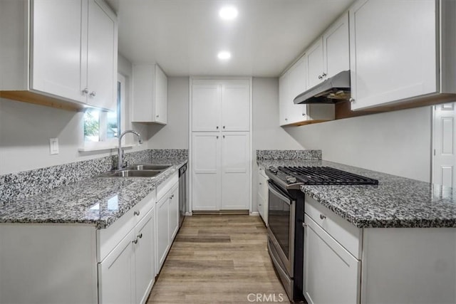 kitchen with sink, light wood-type flooring, stainless steel gas range, white cabinets, and stone countertops