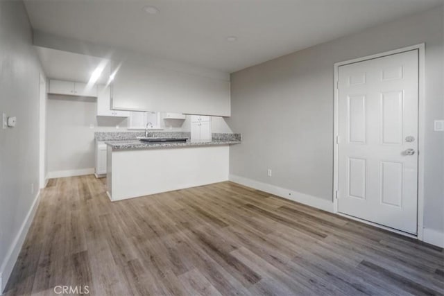 kitchen with white cabinetry, light hardwood / wood-style flooring, kitchen peninsula, and sink