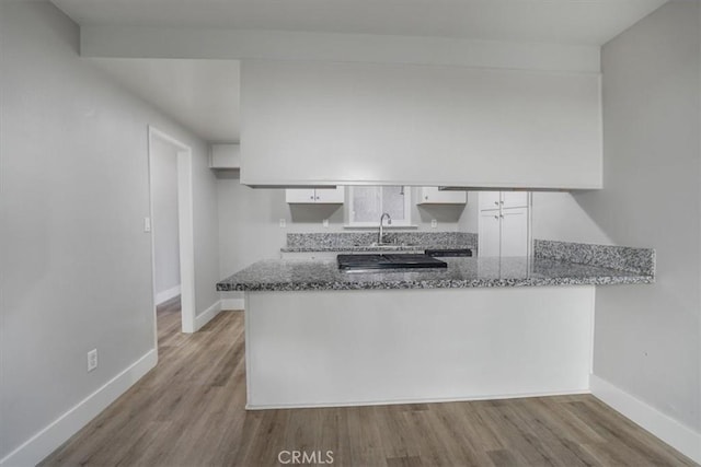 kitchen featuring kitchen peninsula, white cabinetry, light hardwood / wood-style flooring, and stone counters